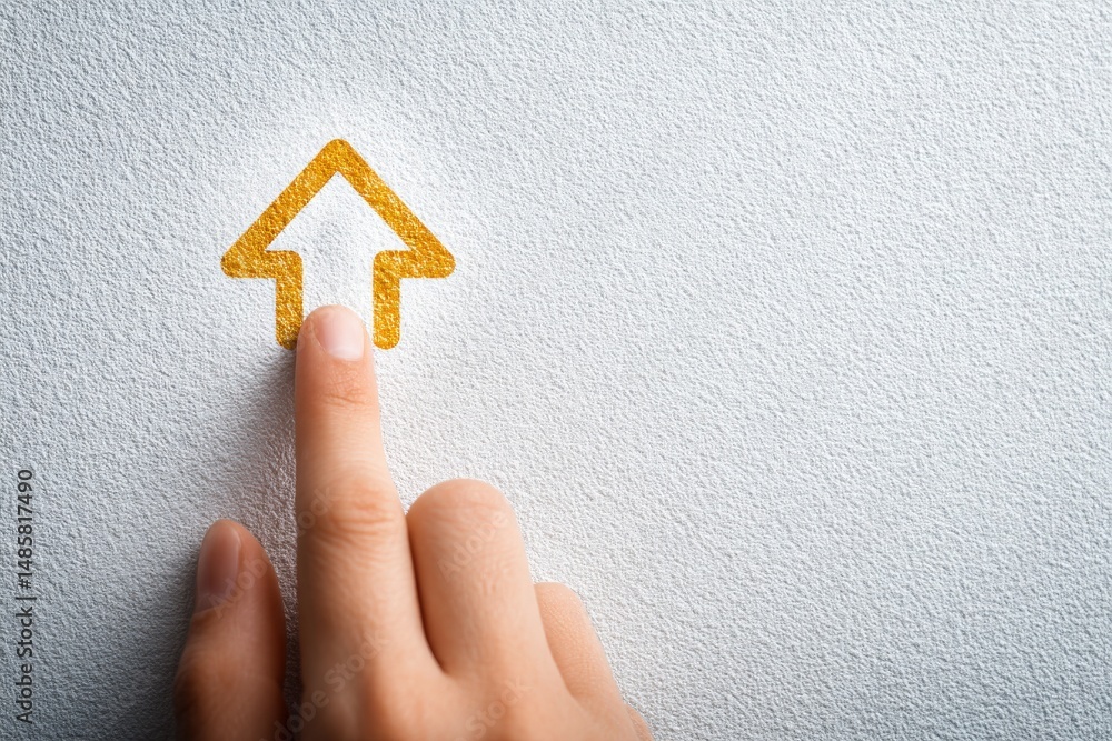 A hand is positioned to touch a stylized golden arrow emblem on a light textured wall. The focus captures the interaction between the human element and the graphic design.