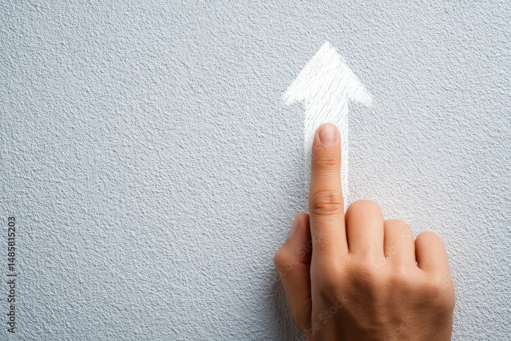 A hand with a finger extended points towards a white arrow sketch on a gray wall. The gesture suggests direction or an upward movement, creating an engaging visual focus.