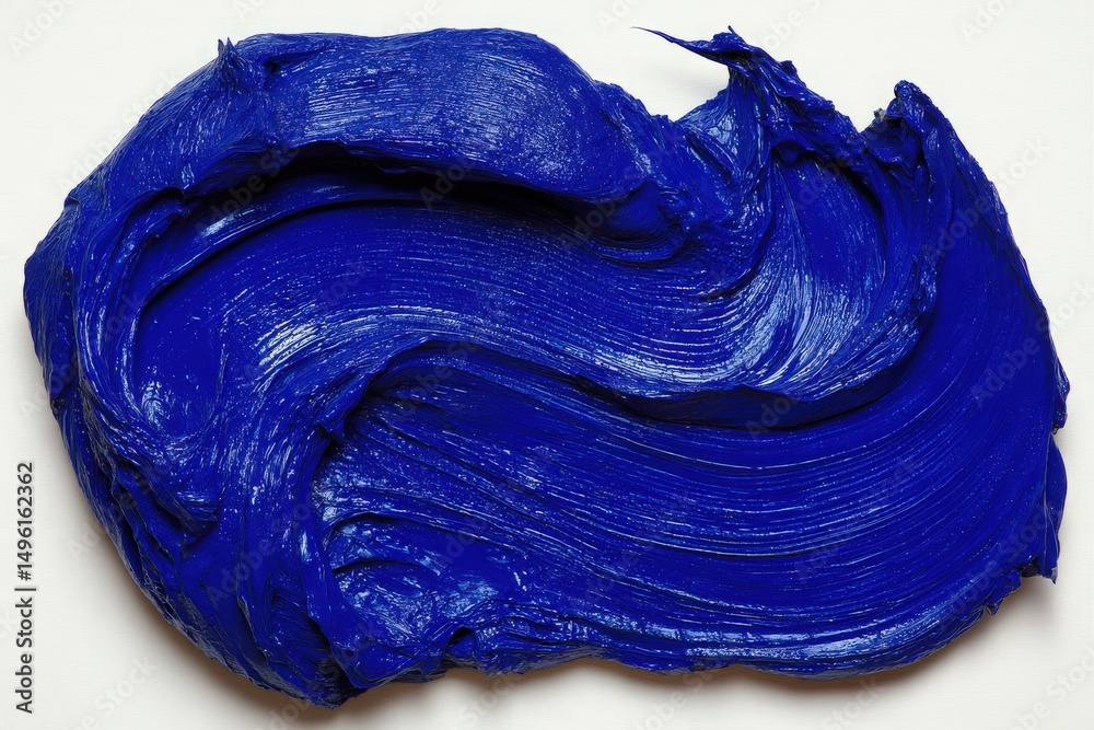 A thick, vibrant blue paint is spread across a smooth white surface, creating a swirling effect. The texture exhibits rich pigment and glossy finish, highlighting artistic potential.