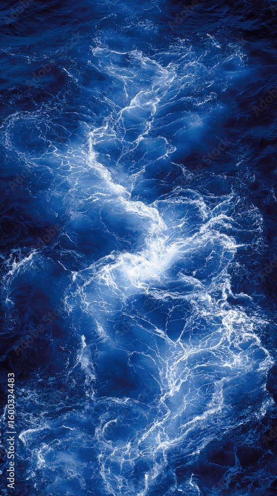 Bright sunlight reflects on the ocean surface, creating intricate patterns of light and dark. The vibrant blue water appears energetic, with waves gently rippling and swirling.