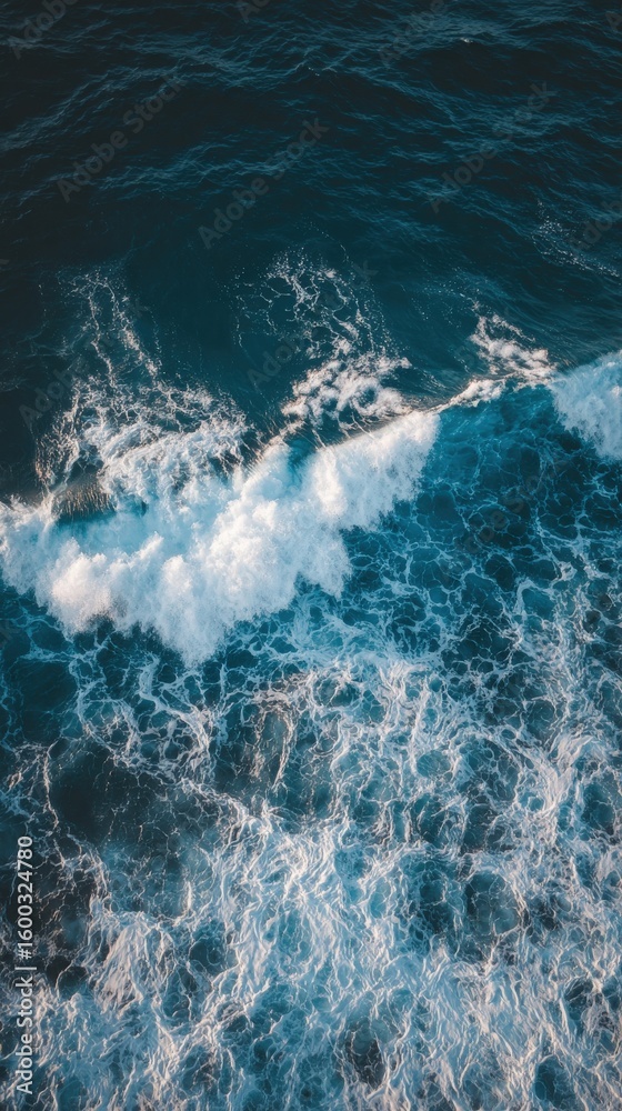 Turquoise waves roll gently against each other, creating frothy white caps. Sunlight reflects off the water, enhancing the tranquil atmosphere of the vast ocean, captured from above.